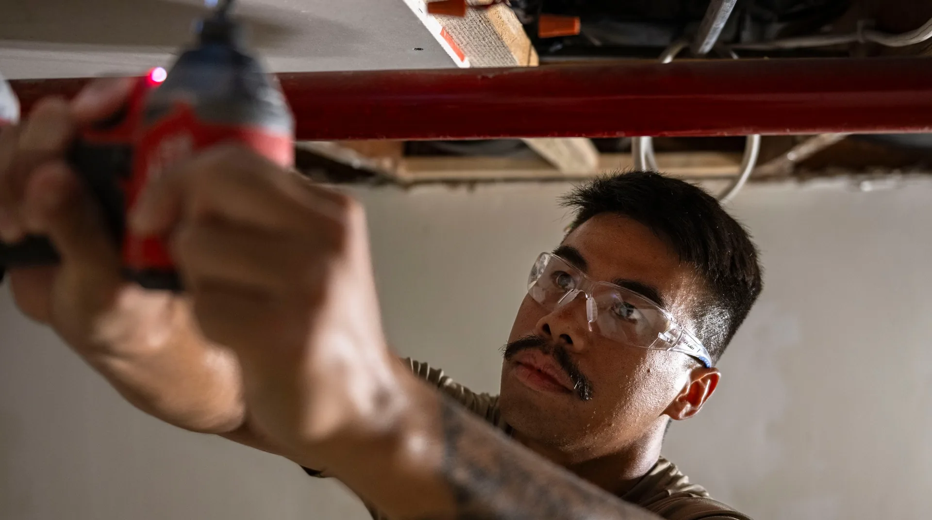 Tradesperson wearing safety glasses fastening drywall during an interior renovation