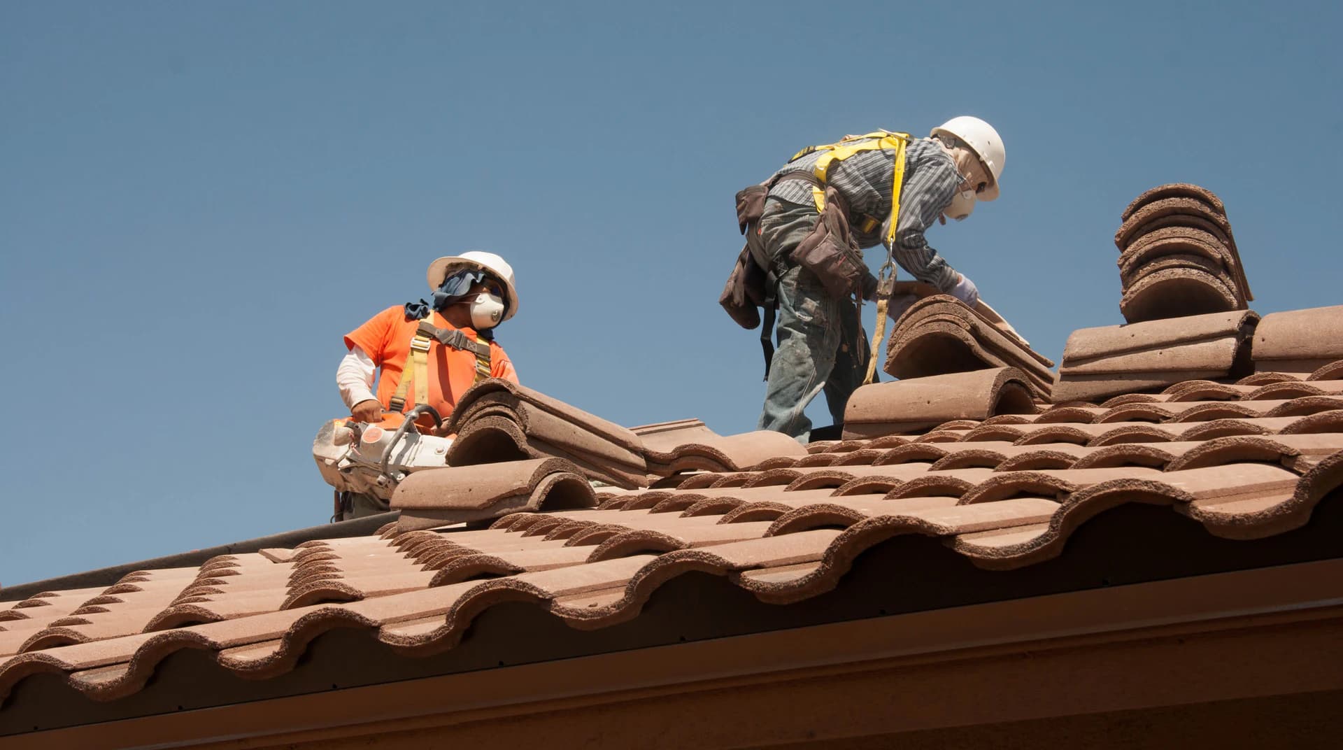 Roofing crew using fall-protection equipment while working on a residential tile roof